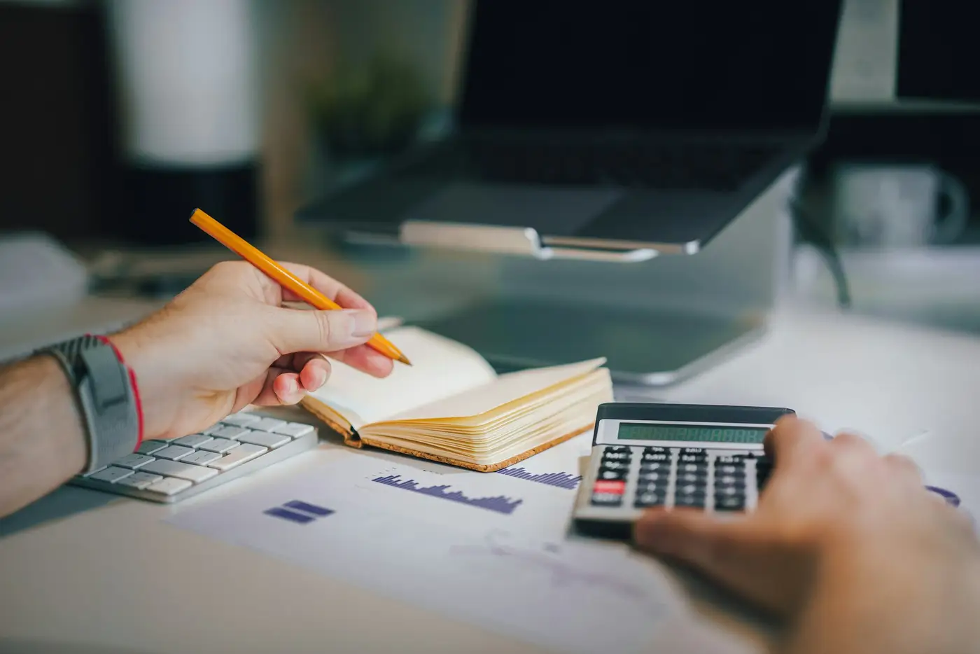 Mains tenant un crayon au-dessus d'un carnet, à côté d'une calculatrice